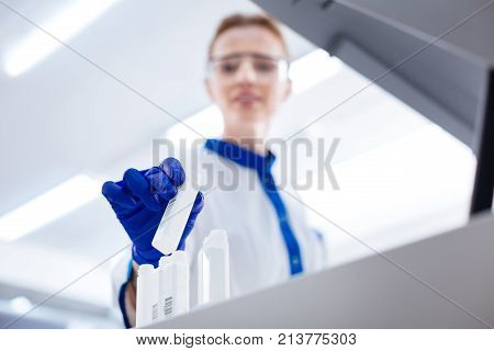 Right place. Glad skillful female scientist wearing blue gloves and placing white plastic container among other containers located in line