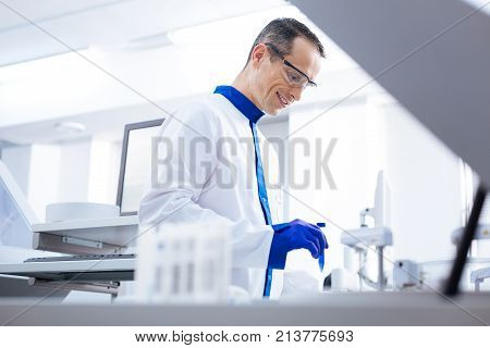 PSA-test. Serious exuberant laboratory assistant  holding test tube while  looking down and smiling happily
