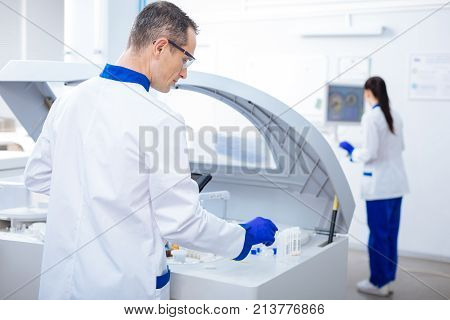 Maybe this. Handsome focused male laboratory assistant searching for glassware while turning with a back  and staring down