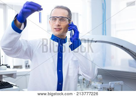 Parental test.  Attractive confident male laboratory assistant  delivering news about the parental test result while carrying test tube and wearing medical glass