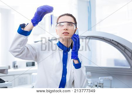 Result examination.  Budding young female researcher  holding test tube and talking on the phone while posing in the lab