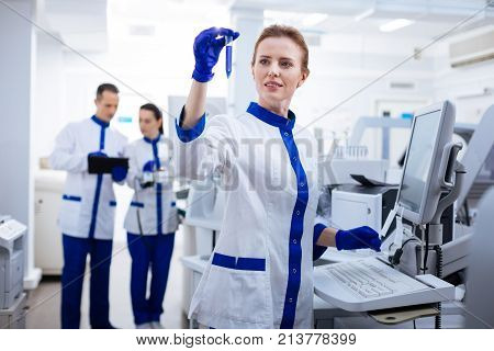 Latest data.  Astonished elegant female scientist  rising test tube  her hand placed above  the keyboard  while standing in the laboratory