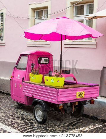 Sibiu Romania October 07 2017 : Pink scooter with closed cockpit and umbrella parked on the Timotei Popovich street in Sibiu city in Romania