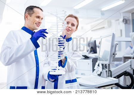 Medical brainstorming.  Attractive pensive male  and female scientists emerging in molecule structure researching  while holding model and standing in the laboratory