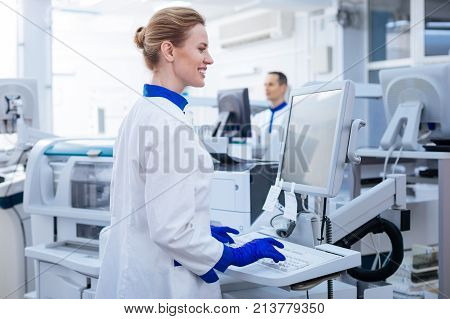 Data base. Attractive smart pleasant male scientist searching for additional information in the computer while putting his hand near the monitor  and posing in the laboratory