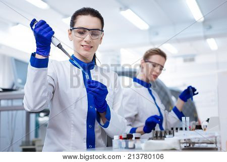 First time. Beautiful genuine female intern using pipette for putting reagent into the test tube which she holding in her hand while wearing blue gloves