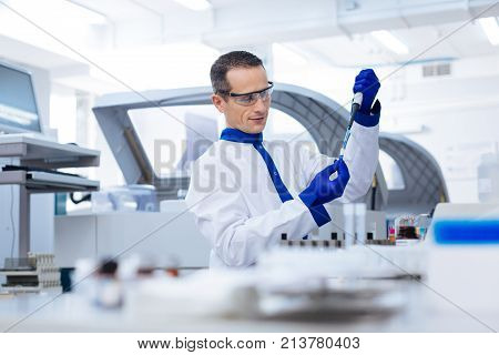 Unbelievable experiment. Confident strong  male scientist performing experiment by putting chemical into the test tube while wearing medical glass and labcoat