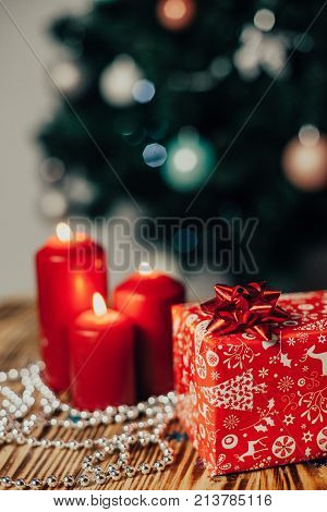 Christmas gift wrapped in gift paper on wooden table on christmas tree bachground with candles