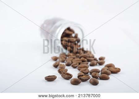 roasted coffee beans poured from clear glass on white background closeup