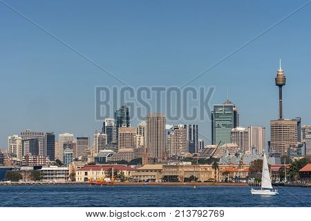 Sydney Australia - March 26 2017: Closeup kind of shot of selection of tall office towers skyline seen off the water under blue sky. White sail boat Navy ship and spires of Saint Mary Cathedral.