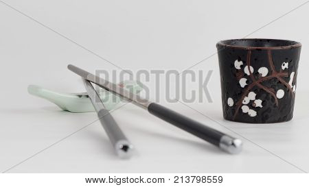 Metal chopsticks on ceramic chopsticks rest and black empty sake-glass. Gray background. Front view