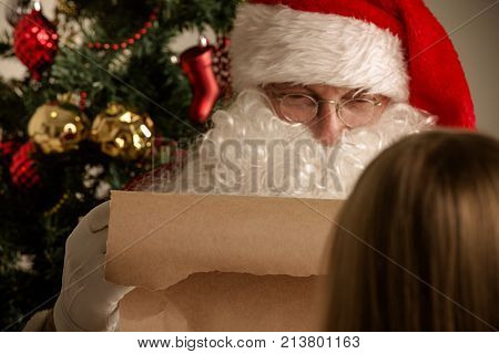 Santa Claus with with list or nice or naugthy list paper with small boy near christmas tree