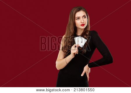 Beautiful caucasian woman in black dress with poker cards gambling in casino. Studio shot on red background. Poker. Two Aces in Hand
