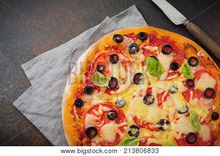Pizza margarita with tomatoes mazarella and slices of olives on a dark concrete or stone background. Traditional Italian cuisine. Selective focus. Top view.