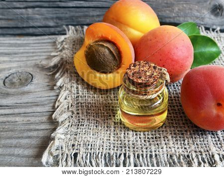 Apricot oil from apricot kernels in a glass jar and fresh ripe apricots on old wooden table.Essential apricot kernel oil for spa,beauty treatment,aromatherapy and bodycare. Selective focus.