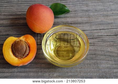 Apricot oil from apricot kernels in a glass bowl and fresh ripe apricots on old wooden background.Essential apricot kernel oil for spa,beauty treatment,aromatherapy and bodycare.Selective focus.