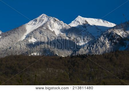 Beautiful scenic green summer landscape of the Main Caucasus ridge with snowy mountain peak tops on blue sky background