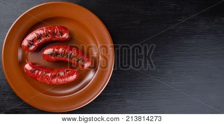 Round clay dish with toasted apetit sausages. Isolated on black background. The concept of traditional food.