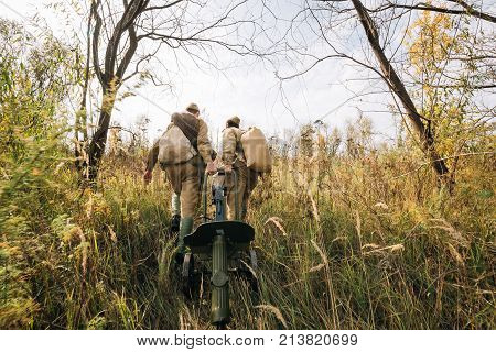 Two Reenactors Dressed As Russian Soviet Red Army Soldiers Of World War II Walking With With Maxim's Machine Gun Weapon In Autumn Meadow, Forest