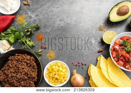 taco ingredients as a frame border background with roasted beef tomatoe salsa corn shells avocado herbs and spices on a dark stone board copy space top view from above selected focus narrow depth of field