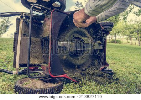 Man cleaning lawn mower blade. Preparing to mow some grass.