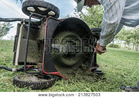 Man cleaning lawn mower blade. Preparing to mow some grass.