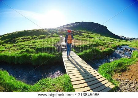 back view of woman traveler with small orange backpack on a walk in the Valley of the river of Hveragerdi Iceland. Hiking Tour of Reykjadalur Hot Springs