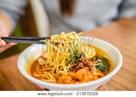 Hand with Chinese chopsticks eating noodle a famous Malaysia prawn noodle cerry soup.