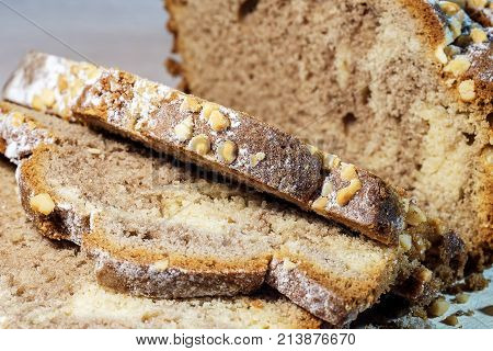 Freshly baked homemade cake decorated on top with powdered sugar cut into slices on a wooden stand on a wooden background. Macro