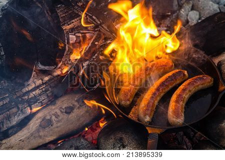 Cooking Sausages In Cast Iron Skillet On Campfire While Camping. Good And Positive Campfire Food.