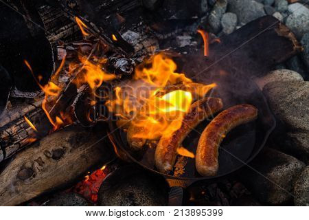 Cooking Sausages In Cast Iron Skillet On Campfire While Camping. Good And Positive Campfire Food.