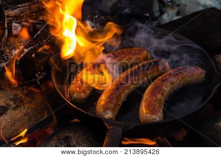 Cooking Sausages In Cast Iron Skillet On Campfire While Camping. Good And Positive Campfire Food.