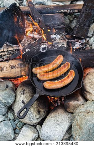 Cooking Sausages In Cast Iron Skillet On Campfire While Camping. Good And Positive Campfire Food.