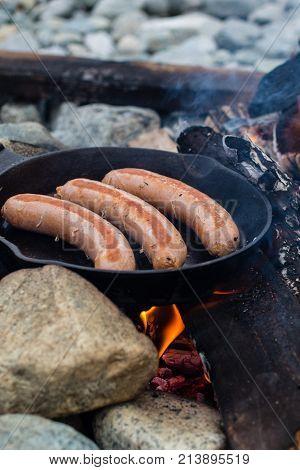 Cooking Sausages In Cast Iron Skillet On Campfire While Camping. Good And Positive Campfire Food.