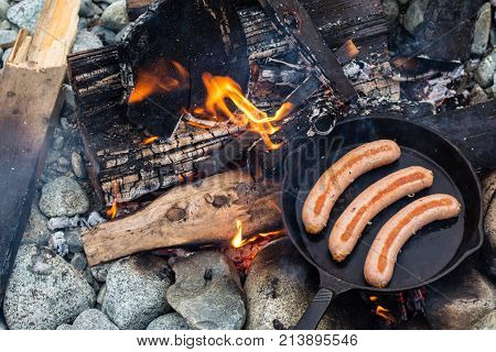 Cooking Sausages In Cast Iron Skillet On Campfire While Camping. Good And Positive Campfire Food.