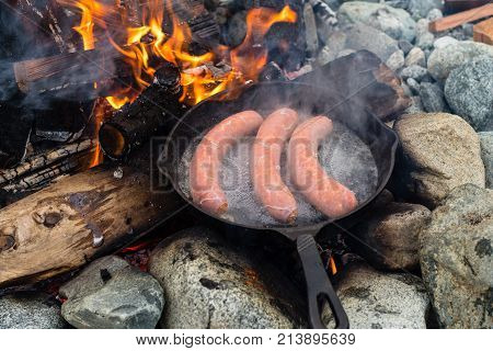 Cooking Sausages In Cast Iron Skillet On Campfire While Camping. Good And Positive Campfire Food.