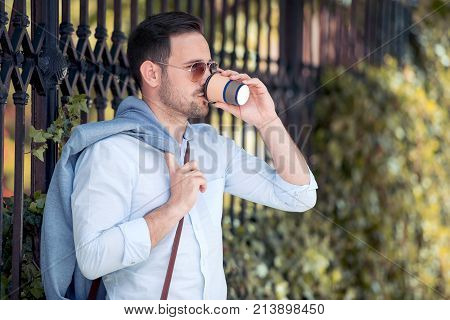 Businesstravel and people concept - young man with coffee to go walking in city.