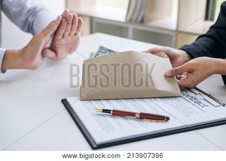 Bribery and corruption concept Businessman refusing receive money in the envelope to agreement contract A bribe in the form of dollar bills.