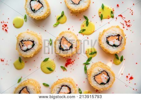 Close up delicious sushi rolls put on white surface with drops of sauce and caviar