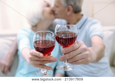 Romantic atmosphere. Two active romantic cute pensioners kissing while holding their drinks