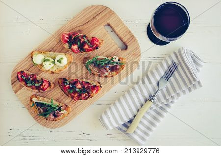 Brushetta set for wine. Variety of small sandwiches served with glass of red wine. Delicious snack appetizer antipasti on party or picnic time. Italian cuisine concept. Slow living. Top view.