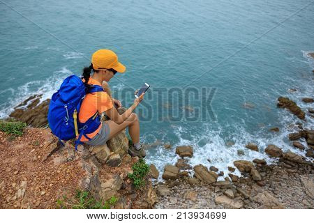 Young woman hiker using smartphone sit on seaside cliff