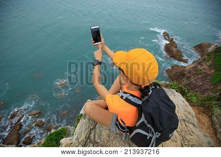 Young woman hiker using smartphone sit on seaside cliff