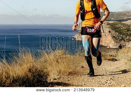 runner athlete running on mountain trail along sea knees in kinesio tape