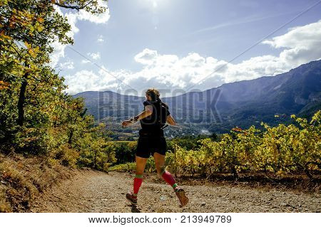back woman runner running mountain trail in sun along vineyards