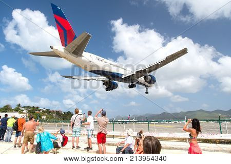 Philipsburg St Maarten - February 13 2016: people watch plane land on island airport on top of maho beach cloudy blue sky. Vacation traveling tourist destination
