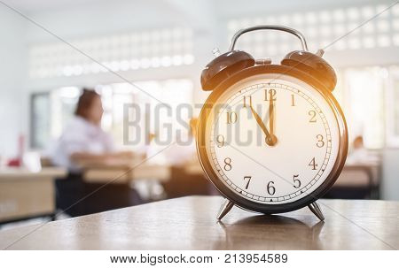 Closeup of Retro alarm clock with ten o'clock on table teacher in blur students exams classroom. Time is indefinite continued progress of existence. Education concept selective focus.
