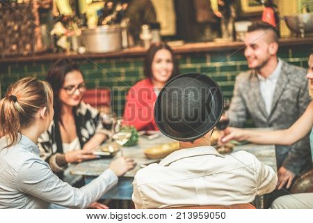Happy trendy friends drinking wine and laughing together inside cocktail fashion bar - Cheerful people having fun doing pre dinner appetizer - Focus on black hat - Contrast filter