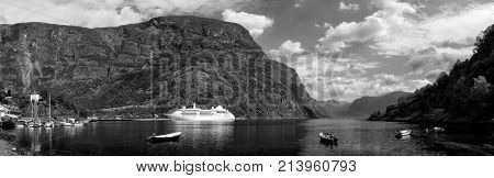 cruiser ship or liner in port fjord bay or harbor calm water surrounded by mountains on rocky sea shore covered with green trees on summer day on cloudy blue sky