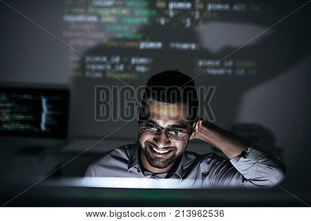 Smiling software developer looking on script on computer screen